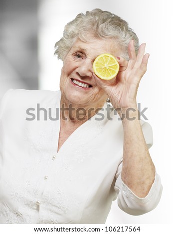portrait of a senior woman with a lemon in front of her eye, indoor