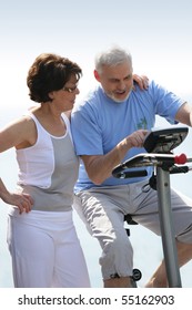 Portrait Of A Senior Woman Next To A Senior Man Making Exercise Bike