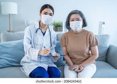 Portrait Of Senior Woman Patient Sit With Physician Doctor In House. Caregiver Therapist Pharmacist Girl Wear Face Mask Visit And Give Service Treatment To Elderly Old Female And Smile, Look At Camera