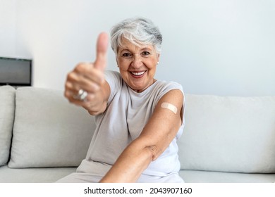 Portrait of a senior woman proudly showing her arm with bandage after getting vaccine. Mature white haired woman sitting against bright background after receiving coronavirus vaccination, thumbs up. - Powered by Shutterstock