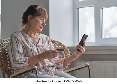 Portrait senior woman shopping online or pays utility bills through the personal account of the online bank, using credit card and smartphone at home.