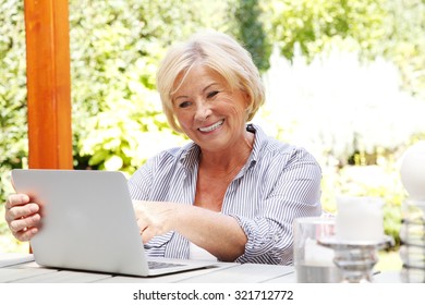 Portrait Of Senior Woman Sitting At Garden With Her Laptop. Smiling Grandmother Enjoys The Convenience Of Banking At Home.