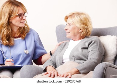 Portrait Of Senior Woman Sitting At Home And Consulting With Middle Age Caregiver. Home Healthcare Nurse Holding In Her Hand Clipboard And Giving Advise While Talking To Elderly Patient. 