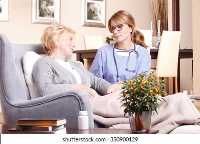 Portrait of senior woman sitting at home in living room while caregiver giving helping hand. 
