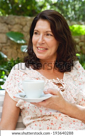 Portrait of a senior woman sitting in a luxury hotel garden on holiday drinking coffee and relaxing on vacation. Mature people drinking hot beverages, outdoors. Senior people lifestyle.