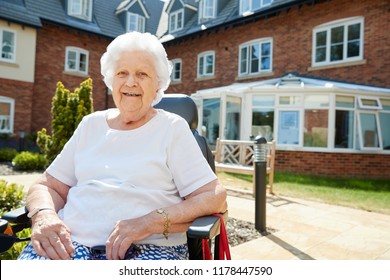 Portrait Of Senior Woman Sitting Outside Retirement Home In Motorized Wheelchair