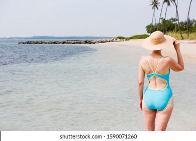 Portrait of a senior woman in a swimsuit at the beach wearing a straw hat - Powered by Shutterstock