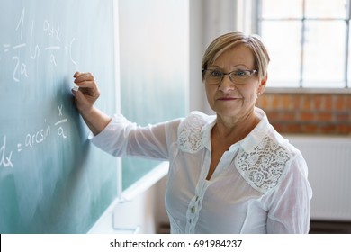 Portrait of senior woman writing mathematical formula on blackboard in classroom