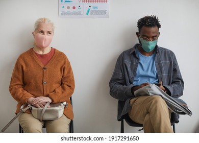 Portrait of senior woman and young African American man waiting in line at clinic or vaccination center both wearing masks - Powered by Shutterstock