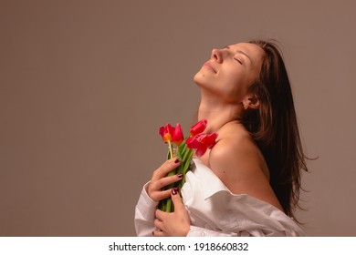 portrait of a sensual girl in profile with flowing hair and bare shoulders closed her eyes stands and dreams holding flowers, on the shoulder on the background beige background, head thrown back


