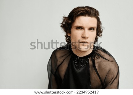 Portrait of sensual non binary man wearing makeup and looking at camera against white, copy space