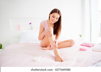 Portrait of sensual, sexy, pretty, stylish, attractive, charming, cheerful, cute, brunette girl using body cream on her dry skin of legs, enjoying softness after lotion, wellness, wellbeing concept