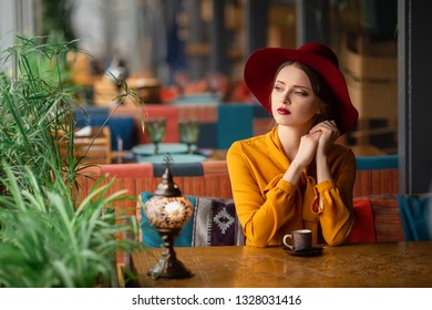 portrait of sensual young girl wearing floppy hat and blouse with bow. Beautiful brunette woman in cafe with cup of coffee