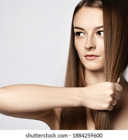 Portrait of sensual young woman holding strand of her long silky hair in her fist demonstrating its strength and health and looking at copy space over grey background. Haircare, beauty, wellness