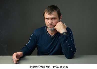 Portrait Of A Serious Adult Man At The Table Talking On A Gray Background Looking At The Camera