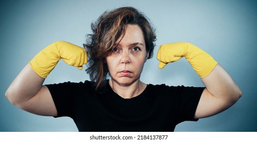 Portrait Of A Serious Adult Woman In A Black T-shirt Shows Muscles On The Background. Woman Cleaning In Yellow Gloves. Vintage Woman Portrait