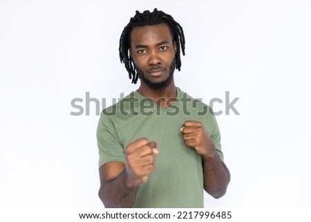 Portrait of serious African American man with clenched fists. Confident young male model with braided dark hair in green T-shirt looking at camera, ready to fight. Strength, self-defense concept.