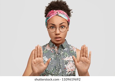 Portrait Of Serious African American Woman Shows Stop Gesture, Asks Be Calm, Refuses Smoking In Company Of Friends, Isolated Over White Background. People, Body Language And Ethnicity Concept