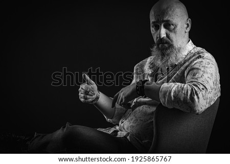 portrait of a serious, bald, bearded man in a T-shirt. With a lush beard looking away, posing on a dark background. Fashion and style. Close up, space for inscription. Black and white photo