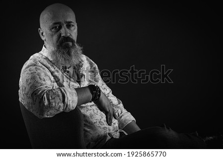 portrait of a serious, bald, bearded man in a T-shirt. With a lush beard looking away, posing on a dark background. Fashion and style. Close up, space for inscription. Black and white photo