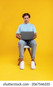Portrait of serious bearded guy sitting on chair using laptop computer, reading news, watching video or movie, working or elearning remotely, isolated on orange studio background, front vertical shot