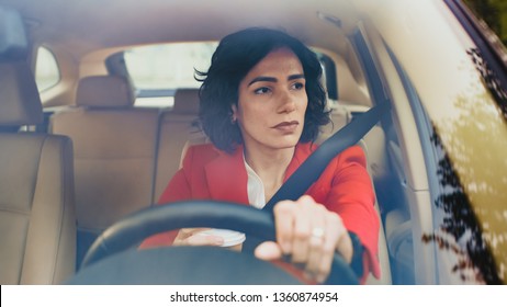 Portrait Of Serious Beautiful Young Woman Driving Car Through Sunny Suburban Area. Camera Shot Made From The Front Windshield.