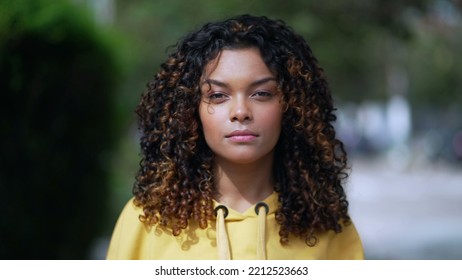 Portrait Of A Serious Black Hispanic Latina Girl With Curly Hair Standing Outside Looking At Camera. African American Young Millennial Woman In 30s Wearing Yellow Blouse