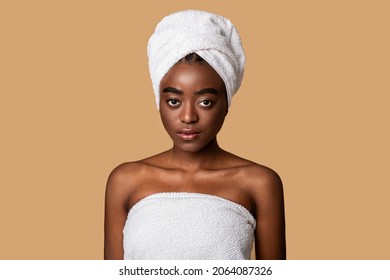 Portrait Of Serious Black Young Woman Wearing White Towel On Body And Head Posing Looking At Camera Standing Isolated Over Pastel Studio Background. Female Headshot Of Confident Black Lady