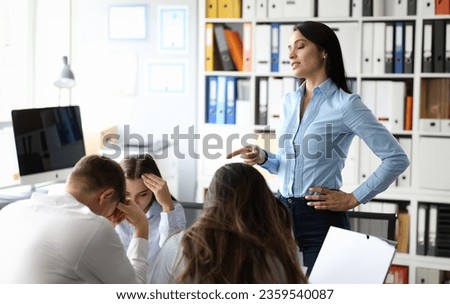 Portrait of serious boss woman in classic shirt pointing finger and giving important directions to colleagues. Upset biz team sitting at table with heads down. Teamwork and teambuilding concept