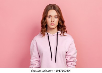 Portrait Of Serious Brunette Teenager Girl In Hoodie Attentively Looking At Camera. Indoor Studio Shot, Isolated On Pink Background