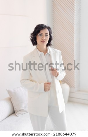 Portrait of a serious business woman in a bright minimalist office. Hold on to the jacket with your hands. Looks confidently at the camera.