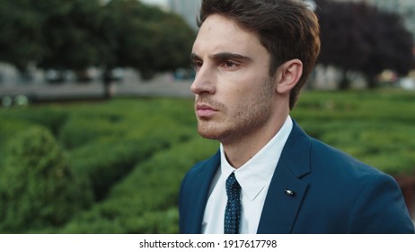 Portrait Of Serious Businessman Walking In City Center. Successful Male Professional Going On Ahead In Street. Handsome Business Man Having Citywalk. Calm Man Walking Past Public Garden.