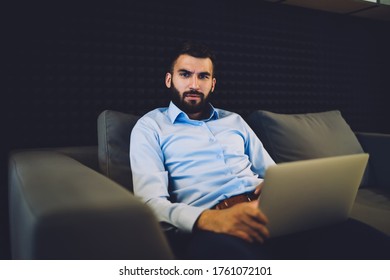 Portrait Of Serious Caucasian Employer Sitting At Comfortable Couch And Looking At Camera Confused With Received Web Information, Bearded Professional Expert With Modern Laptop Computer Posing