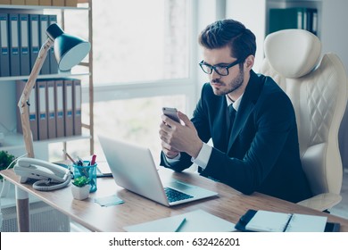 Portrait of serious concentrated man in suit and glasses sitting at the desktop and dialling the phonenumber
