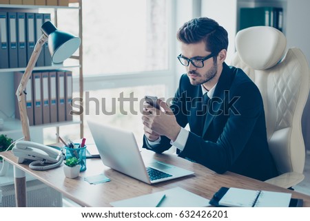 Portrait of serious concentrated man in suit and glasses sitting at the desktop and dialling the phonenumber