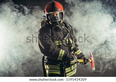 portrait of serious and confident caucasian fireman stand holding hammer, wearing special protective uniform in the smoky background