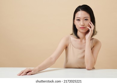 Portrait Of Serious Confident Young Woman Touching Face And Looking At Camera