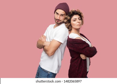 Portrait Of Serious Couple Of Friends In Casual Style Standing Back To Back, Crossing Arms And Looking At Camera With Proud Face. Isolated, Indoor, Studio Shot, Pink Background