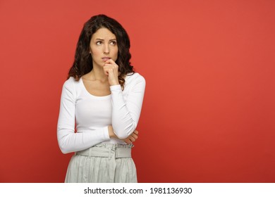 Portrait Of Serious Doubtful Woman Looking Up Thinking Pensive And Confused. Young Curly Girl In White Outfit Isolated On Red Background. Concerned Upset Female In 30s Bite Lips In Doubts And Thoughts