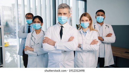 Portrait Of Serious Experienced Different Mixed-races Healthcare Workers Doctors And Physicians In Medical Masks Posing In Clinic Looking At Camera, Quarantine Concept, Team Colleagues