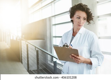 Portrait Of A Serious Female Doctor Holding Her Patient Chart In Bright Modern Hospital