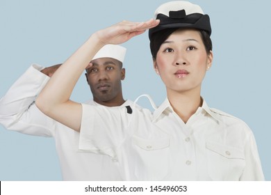 Portrait Of Serious Female US Navy Officer And Male Sailor Saluting Over Light Blue Background