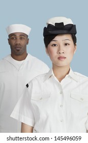 Portrait Of Serious Female US Navy Officer In Front Male Sailor Over Light Blue Background