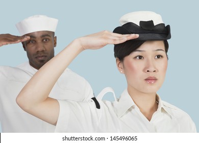 Portrait Of Serious Female US Navy Officer And Male Sailor Saluting Over Light Blue Background