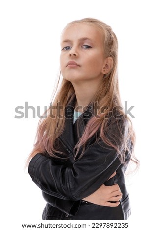 Portrait of serious five year old girl arms crossed over looks at cameraisolated on white background. Blonde child with irritated face in black leather jacket and blue jeans posing in studio.