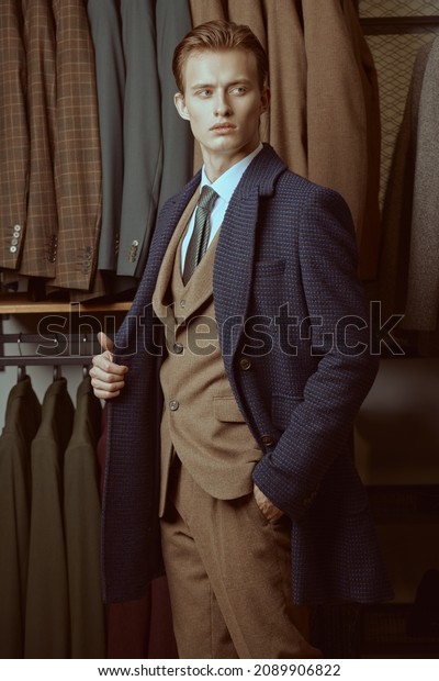 Portrait of a serious\
handsome business person dressed in smart three-piece suit and coat\
standing in the background of luxury classic suits in a store.\
Men\'s fashion and\
style.