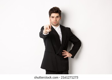 Portrait of serious handsome man in business suit, showing one finger to prohibit or decline something, telling to stop, disagree with you, standing over white background
