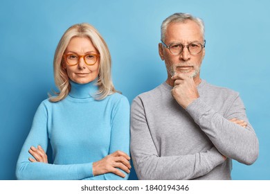 Portrait Of Serious Husband And Wife Pose Together In Casual Clothes Make Photo For Long Memory. Self Confident Retired Colleague Stand In Assertive Pose Next To Each Other Against Blue Background