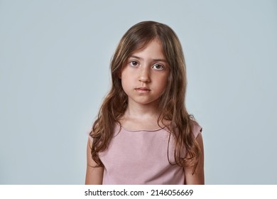 Portrait Of Serious Little Girl Looking At Camera. Partial Image Of Cute Caucasian Female Child Wearing Pink T-shirt. Childhood Concept. Isolated On White Background. Studio Shoot. Copy Space