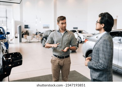 Portrait of serious male client talking to professional car dealer in business suit in dealership discussing automobiles looking at luxurious new model. Concept of choosing and buying new auto. - Powered by Shutterstock